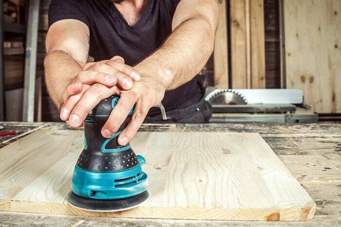 closeup of woodworker using random orbital sander