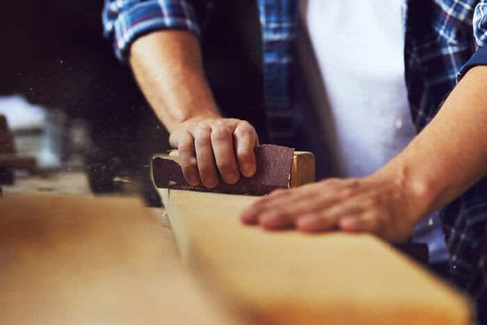 closeup of someone sanding a peice of wood using a sandpaper block