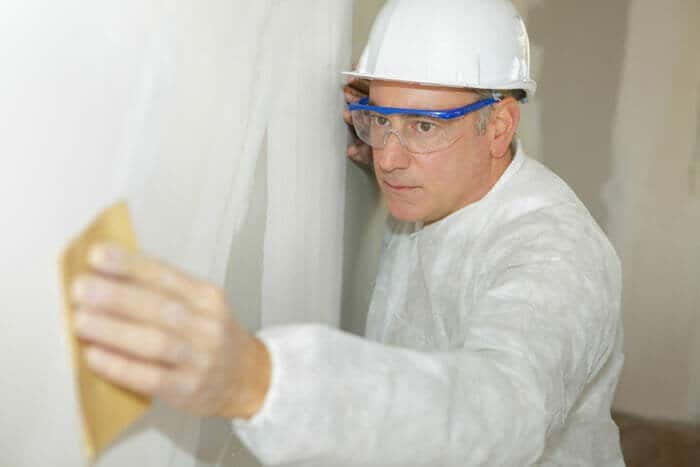 contractor sanding the drywall whilst wearing safety goggles