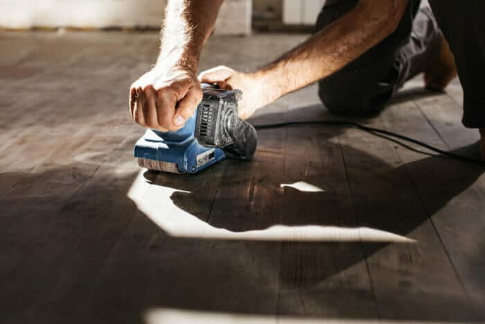 a man sanding a hardwood floor using an orbital sander